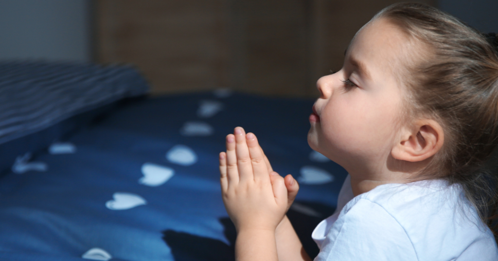 Little girl kneeling beside her bed praying for a good night's rest.